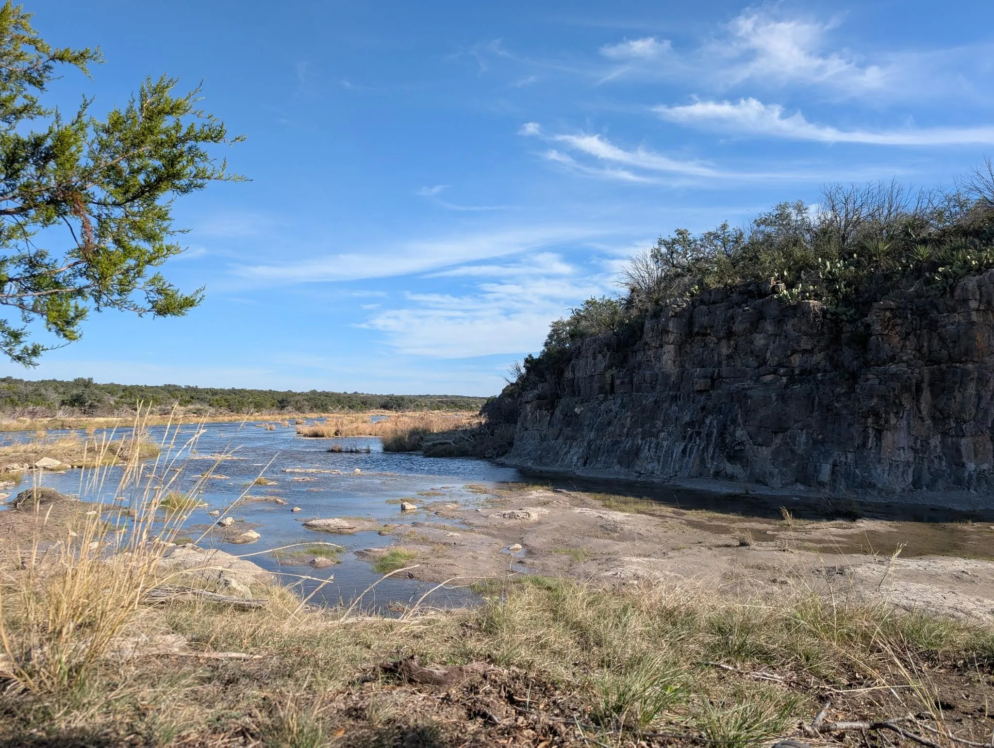 A shallow rocky river below a limestone bluff