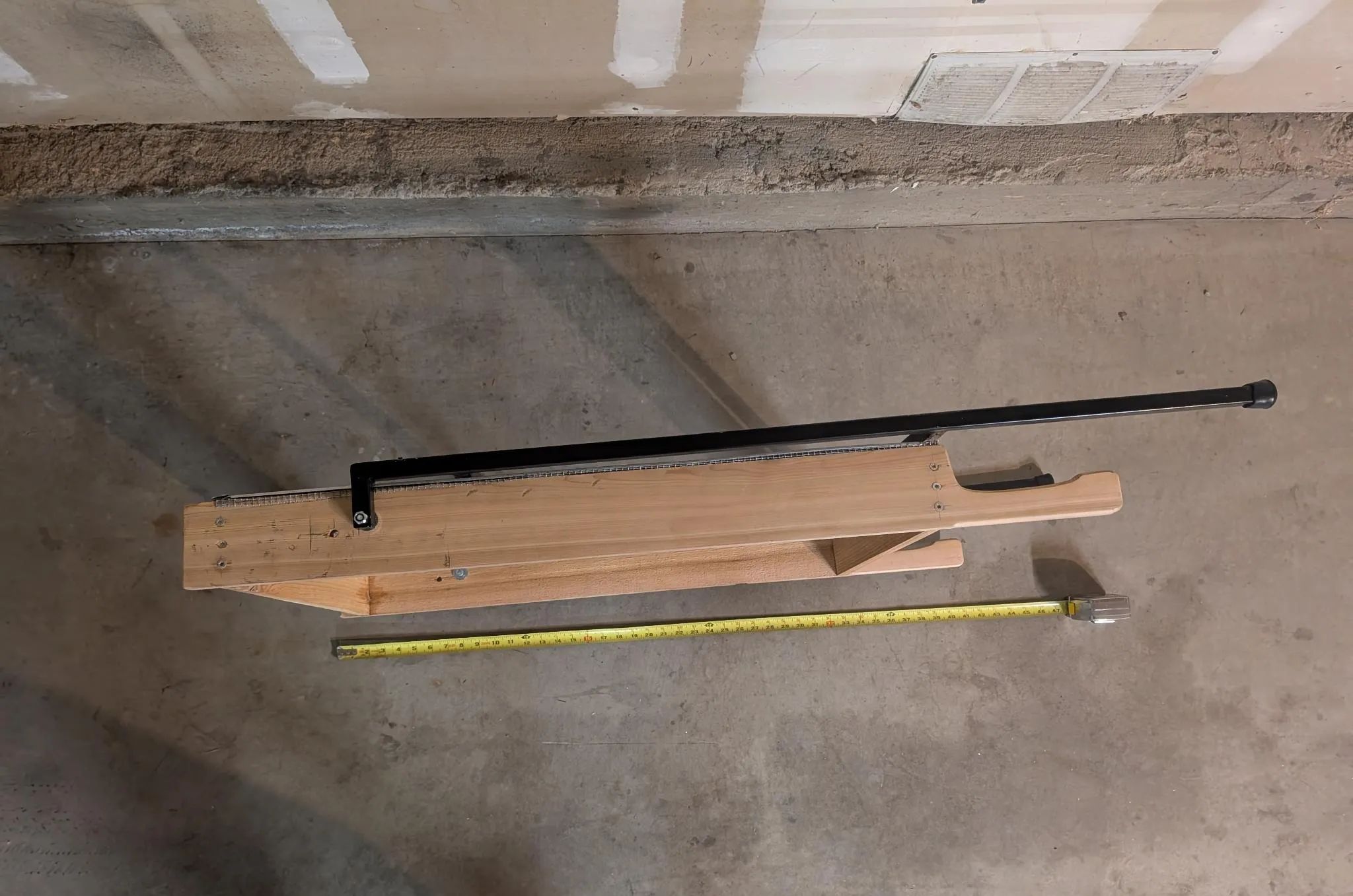 The screen folded flat on a concrete floor with its legs collapsed alongside and a tape measure showing its length